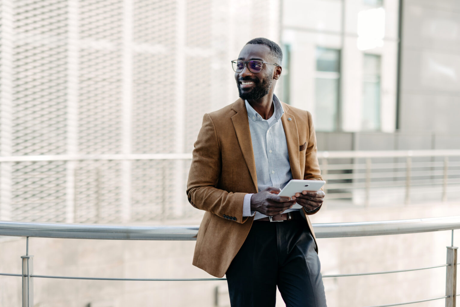 Man leaning on railing with a tablet outdoors
